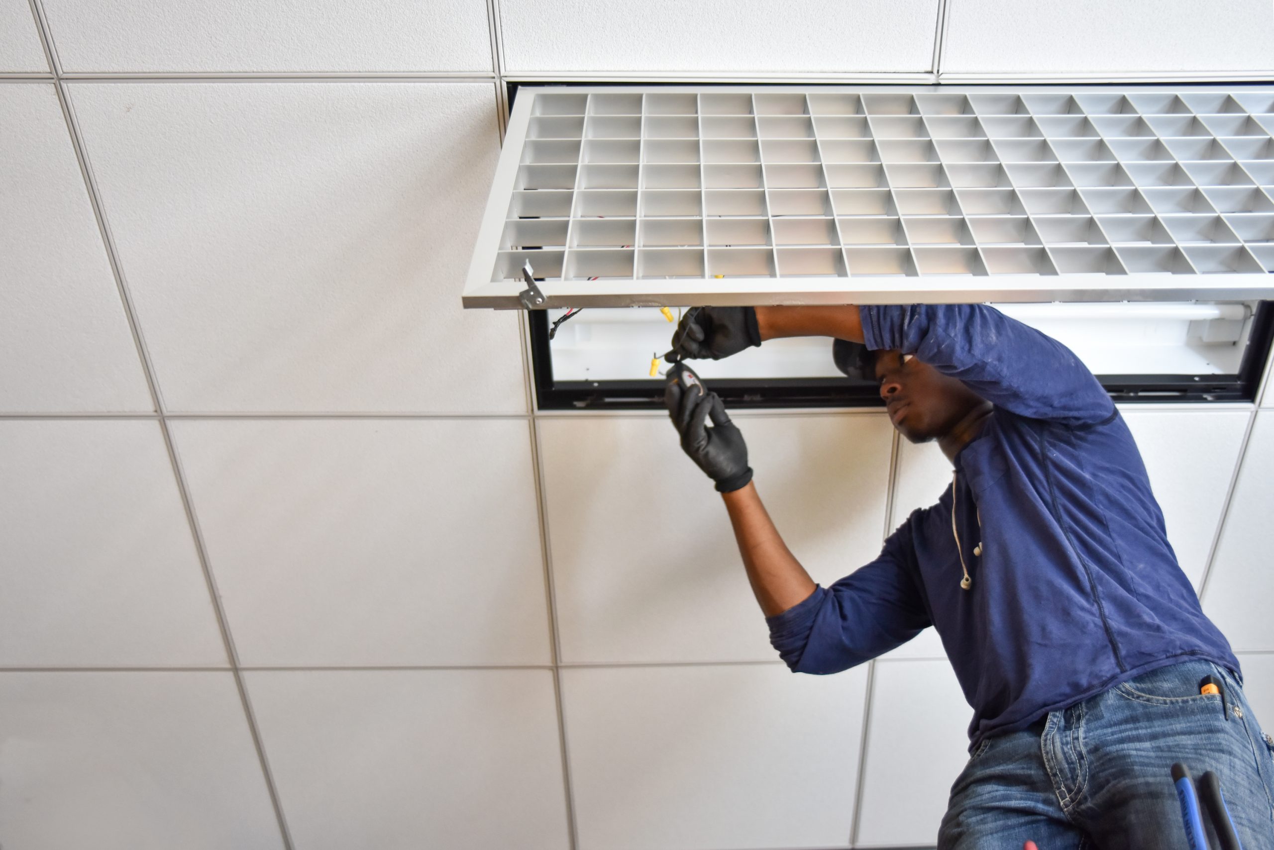A man works on the lighting fixture on the ceiling.
